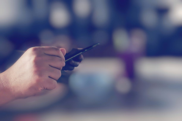 亚洲男子的手握智能手机与散焦(散焦)背景;软焦点图像在电影的颜色。图片下载