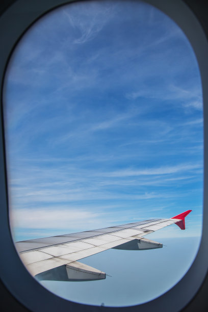 窗外一架飞机的机翼，飞机在蓝天的云朵之上飞行。图片下载