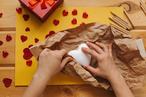 女孩拿着一个心形的符号，用牛皮纸包好，准备送给别人。附近有各种象征这一事件的物品。图片下载