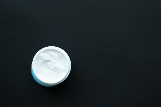 面部或身体用的奶油放在白色容器里，蓝色盖子，黑色背景。医疗保健。spase副本。前视图中,以上。图片下载