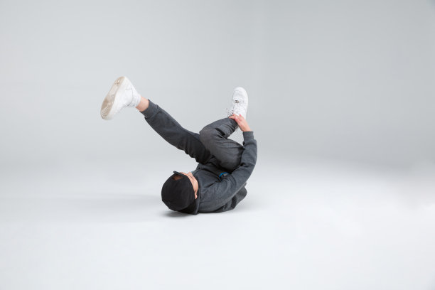 一个小男孩蜷缩着双腿躺在地上跳舞。在一个灰色的背景。图片下载