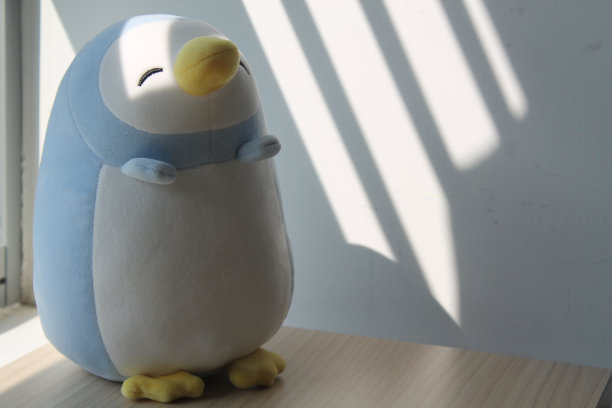 企鹅玩具坐在窗前的阴影里图片下载