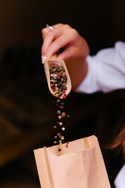 木勺上放有颜色的胡椒。用勺子盛满胡椒粉。女人的手把胡椒放在纸袋里。图片下载