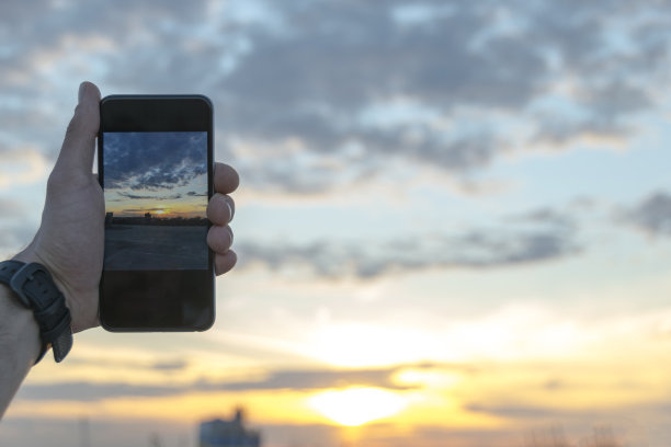 夏日傍晚，一名男子用智能手机拍摄日落。图片下载