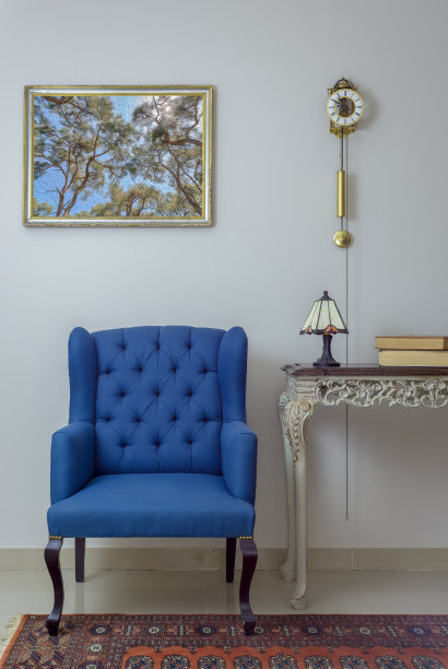 室内由复古的蓝色扶手椅、复古的米色木制桌子、台灯、书籍和钟摆组成，白色墙壁上，瓷砖米色地板和橙色华丽的地毯图片下载