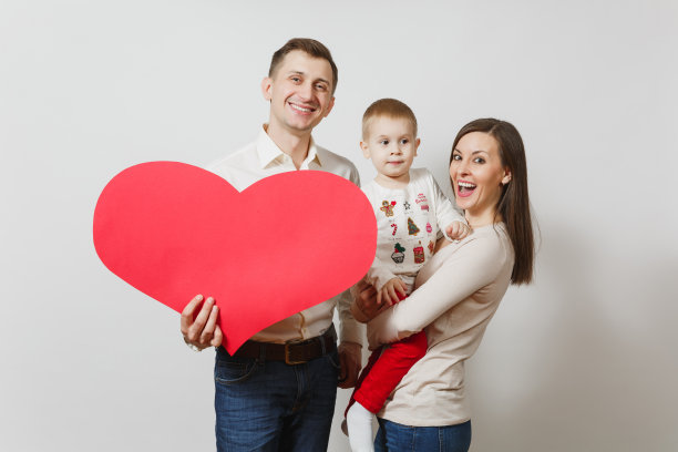 快乐微笑的年轻男子，妇女抱着，拥抱着可爱的小男孩与大红心孤立在白色的背景。父亲，母亲，小儿子。父母、家庭、父母和孩子的概念图片下载