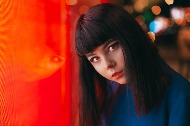 年轻的日本女孩站在霓虹灯旁边，对着照相机摆姿势。红色和蓝色灯光，夜晚，街道图片下载