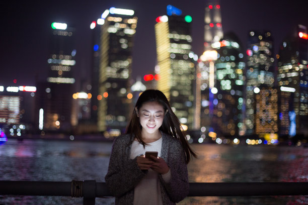 年轻的亚洲妇女在现代城市玩手机图片下载