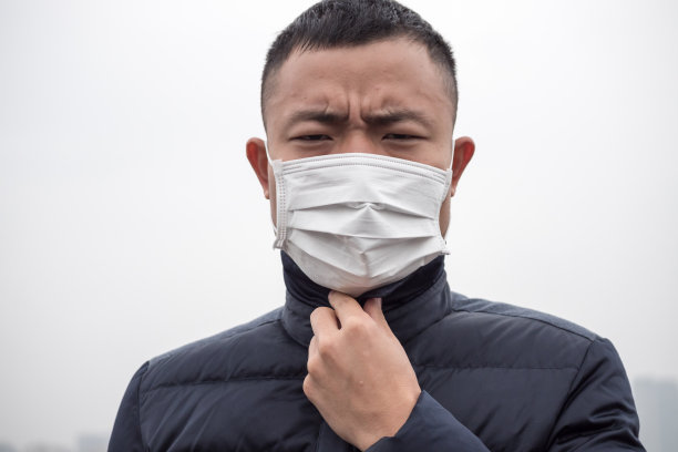 一个年轻的亚洲人戴着白色面具站在雾天里素材图片