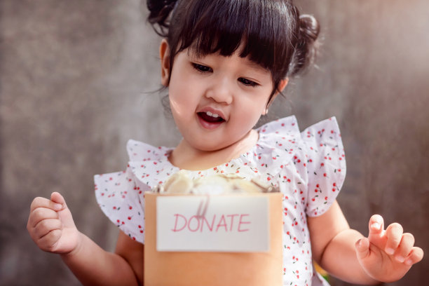 孩子与捐赠概念。快乐2岁的孩子微笑和看钱硬币在一个捐赠箱图片下载