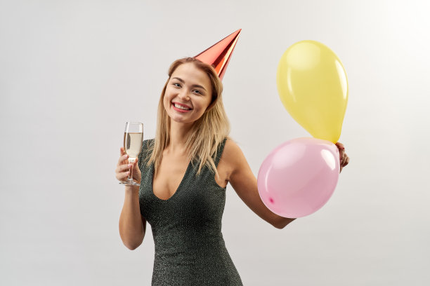 年轻迷人的微笑女孩穿着裙子，头上戴着节日帽，手里拿着气球，亲切地微笑着，看着镜头图片下载