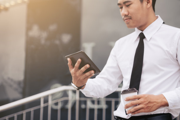 英俊的商人拿着平板电脑，在早上看电子邮件。图片下载
