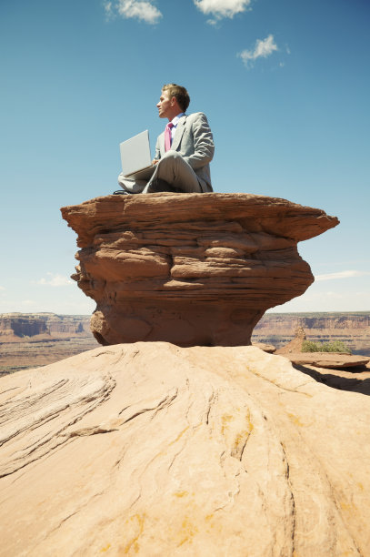 商人坐在岩石台面上用笔记本电脑思考图片下载