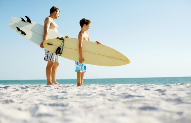 父子俩带着冲浪板站在海滩上图片下载