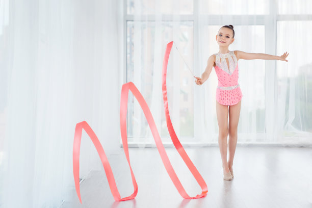 漂亮的小体操女孩穿着粉红色运动服，用艺术丝带做艺术体操运动图片下载