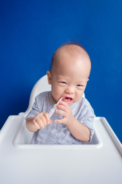 可爱的亚洲蹒跚学步的小男孩戴着围嘴，拿着牙刷，坐在高椅子上刷牙图片下载