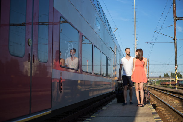 幸福的年轻白种夫妇走在火车旁边，拉着行李箱，穿着休闲的夏装图片下载