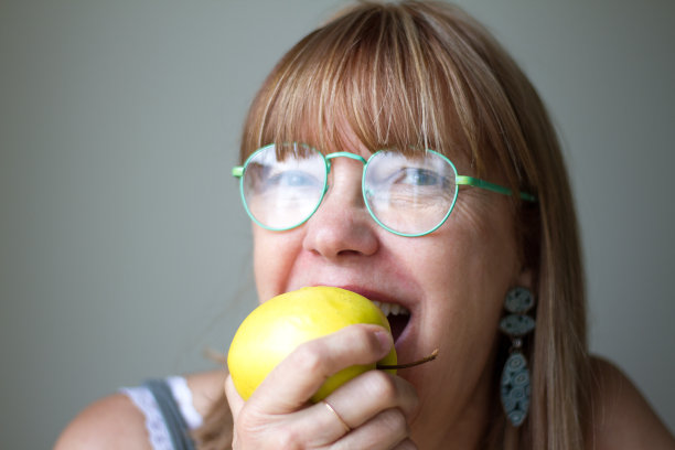 戴绿眼镜的快乐女人咬着黄色的苹果图片下载