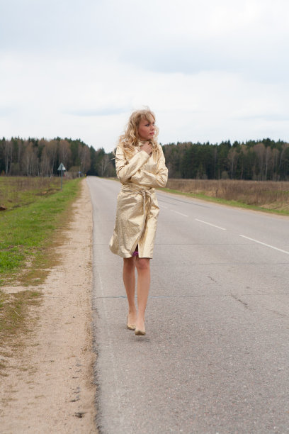 金发的女模特穿着金色的外套和紫色的裙子走在乡间的小路上图片下载