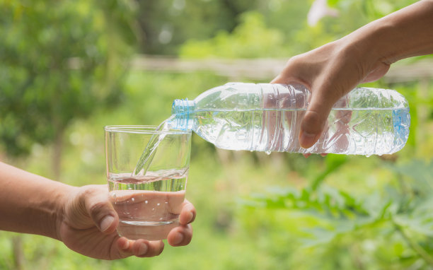以自然为背景，女性用手将水从瓶子倒向玻璃杯图片下载