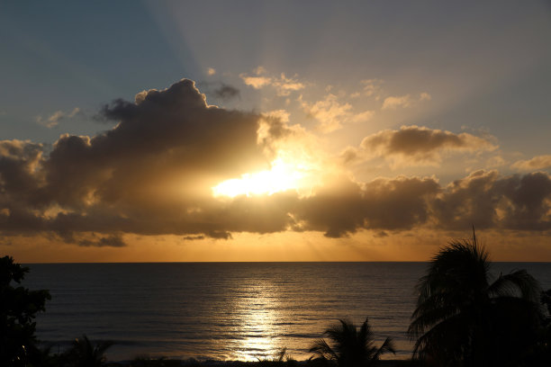 在垂直照片中，清晨的阳光从云层后面出来，在平静的海面上反射图片下载