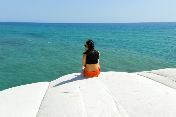 年轻女子坐在悬崖上，眺望热带海洋图片下载