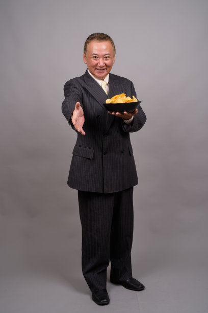 在灰色的背景下，一个成熟的亚洲商人拿着一碗薯片图片下载