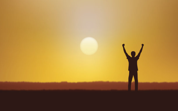 在日落天空的背景下，一个快乐的人的剪影高举过头顶站在田野上图片下载