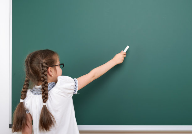 女学生在黑板上用粉笔写字，留白区域，教育概念素材图片