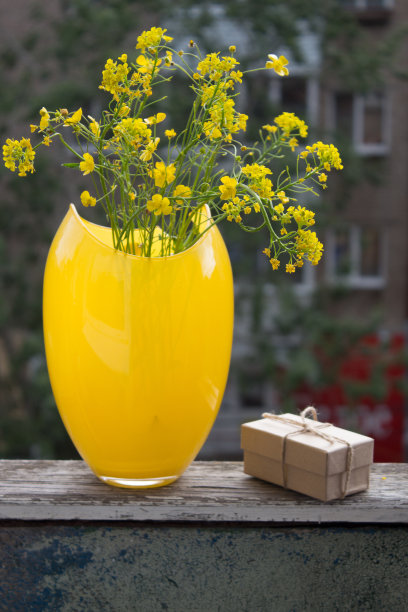 花瓶里有一束黄色的花。礼盒和野花摆放在阳台的木栏杆上。图片下载