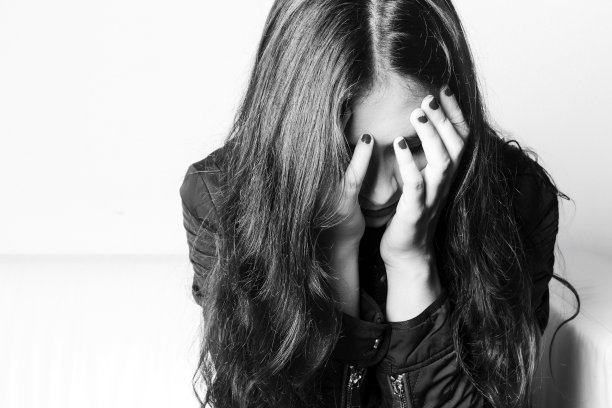 悲伤的黑发女孩，手捂着脸，坐在沙发上。图片下载