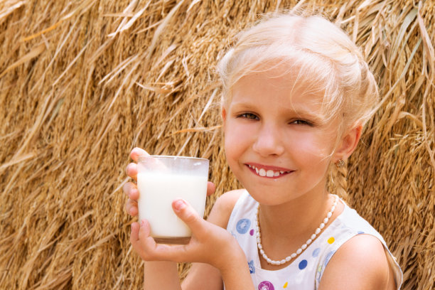 在农场干草堆的背景下，女孩从一个杯子里喝着牛奶。图片下载