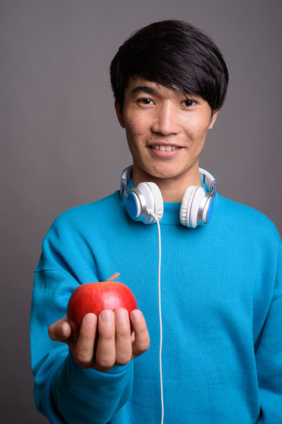 年轻亚裔男子戴着蓝色耳机，以灰色背景为背景的影棚照片图片下载
