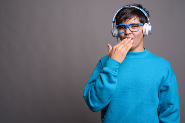 戴蓝色毛衣、蓝色眼镜和耳机的年轻亚洲少年影棚照片图片下载