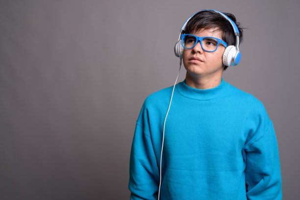 戴蓝色毛衣、蓝色眼镜和耳机的年轻亚洲少年影棚照片图片下载