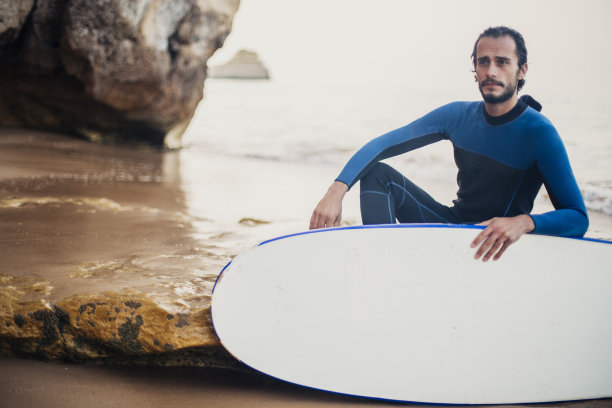 一个男人拿着冲浪板坐在海滩上图片下载