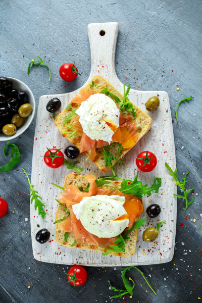 荷包蛋配烤吐司，烟熏鲑鱼，橄榄和蔬菜放在白板上。健康的早餐素材图片