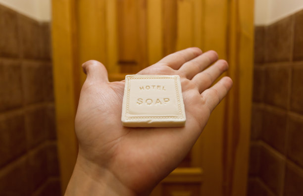 在酒店房间里，一名游客的一只手拿着客房浴室里洗漱用品中的小块沐浴皂图片下载