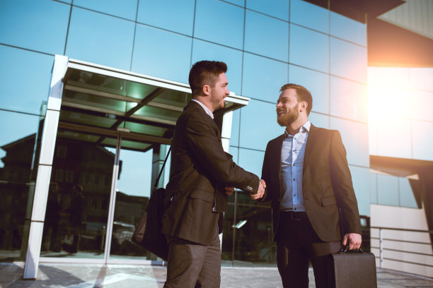 两个商人同事微笑着在办公室前握手图片下载