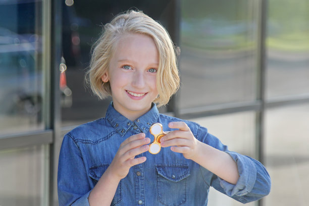 美丽开朗的女学生在玩金色指尖陀螺。儿童和成人的流行玩具。图片下载