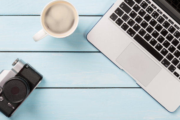 复古相机，现代笔记本电脑和一杯卡布奇诺咖啡在蓝色的木制背景。摄影师工作场所。为你的文本复制空间。图片下载