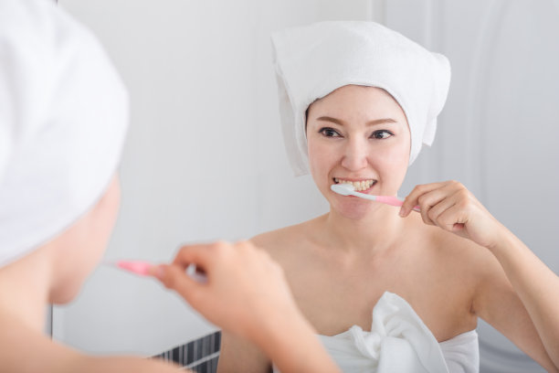 一个穿着浴巾的女人在浴室里用镜子刷牙图片下载