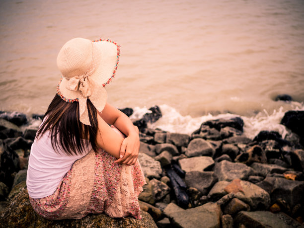 复古的孤独和沮丧的女人坐在大海前在一个秋天的一天荒芜的海滩。图片下载