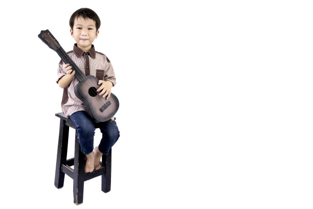 在孤立的白色背景下，男孩在木椅上弹吉他图片下载