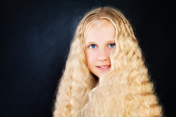 年轻美丽的女孩与长长的金发。金发小女孩与卷曲的头发在黑暗的背景图片下载
