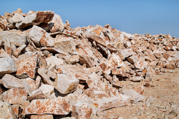 棕色的花岗岩。一大堆用于建造的岩石和在夏天的蓝天下堆成一堆的巨石。采石场的一大堆石灰石。砂砾和建筑材料堆。图片下载