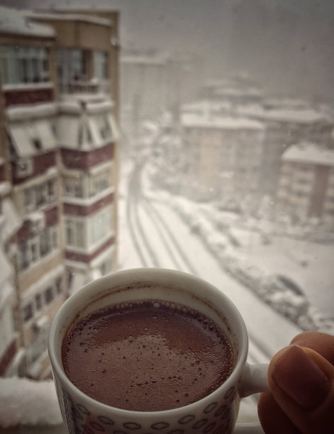 手捧一杯咖啡顶着城市的风景下着冬天的雪图片下载