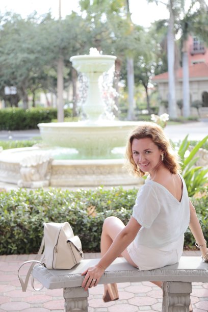 年轻女子坐在喷泉前的长椅上。图片下载