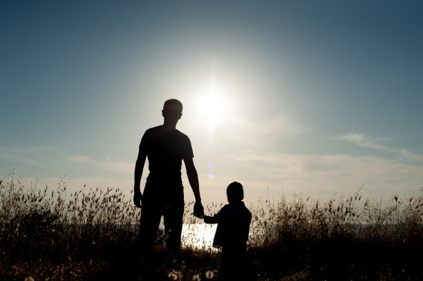一个成年男子和一个小男孩的剪影映衬着海面上的夕阳素材图片