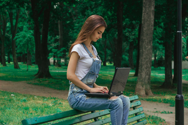 年轻的黑发女孩坐在长凳上，用笔记本电脑工作图片下载